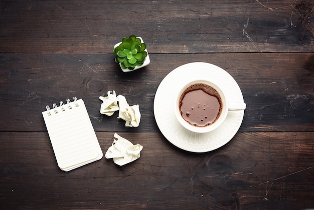 Tasse en céramique blanche avec café noir sur table en bois marron, vue du dessus