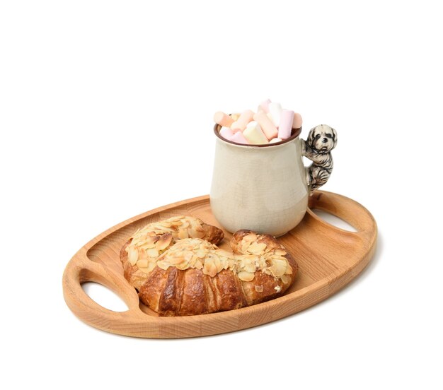 Tasse en céramique avec cacao et guimauves, croissant cuit au four sur une assiette en bois, nourriture sur surface blanche