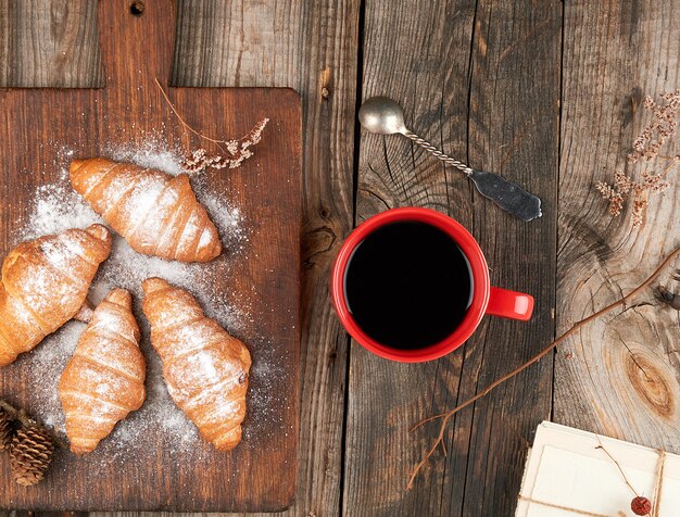 Tasse en céramique rouge avec café noir et planche à découper en bois avec croissants au four