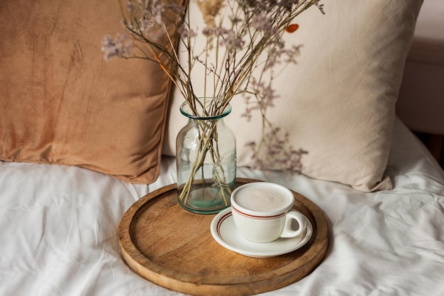 Tasse chaude de cappuccino sur plateau en bois sur le lit petit déjeuner bouquet de fleurs séchées Paysage de printemps Maison confortable Beige couleurs naturelles