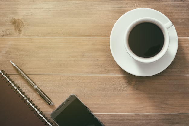 Tasse chaude de petit-déjeuner matin café Americano avec carnet, stylo et téléphone portable sur backgrou en bois