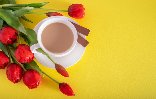 Une tasse de chocolat au lait au café chaud du matin et un bouquet de tulipes pinklilac sur fond jaune