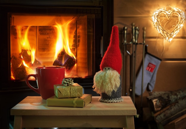 Tasse de chocolat chaud ou de cadeaux de café et gnome de Noël sur une table en bois vintage devant la cheminée