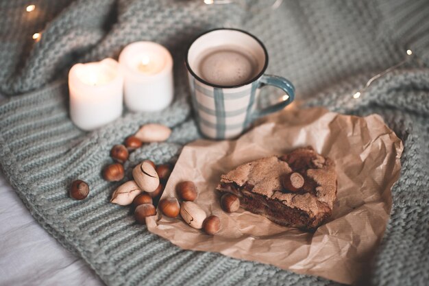 Tasse de chocolat chaud avec un délicieux morceau de tarte, des noix et des bougies allumées sur un tissu tricoté en gros plan au lit. Vue de dessus. Bonjour. Petit-déjeuner. Saison des vacances d'hiver. Nature morte.