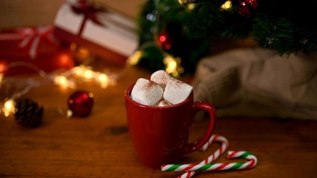 Une tasse de chocolat chaud avec de la guimauve fondante sur une table en bois avec un sapin de Noël et un décor