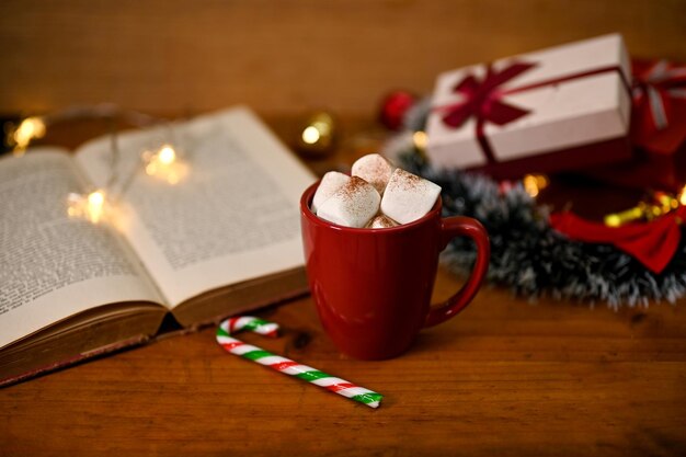 Une tasse de chocolat chaud avec de la guimauve sur une table en bois avec un livre vintage et un décor de Noël