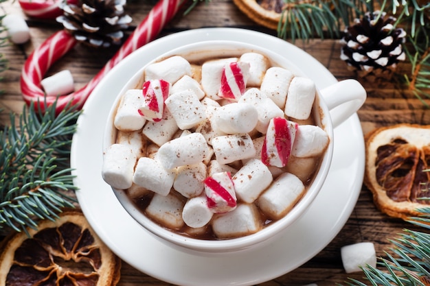 Une tasse de chocolat chaud avec des guimauves. Sapin de Noël et décorations, canne caramel et noix d'oranges Fond en bois