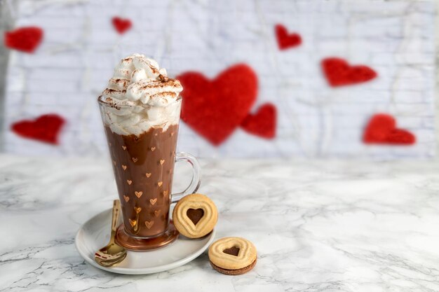 Tasse de chocolat à la crème et biscuits aux coeurs sur fond de coeurs sur marbre blanc