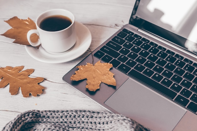 Tasse de composition confortable d'automne de feuilles de café et d'ordinateur portable sur une table en bois blanche