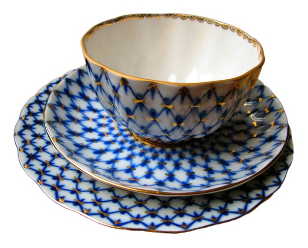 Une tasse et deux soucoupes avec un beau motif bleu et or isolé sur un gros plan blanc