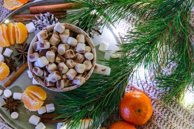 Tasse avec du cacao d'hiver chaud et des guimauves mandarines branche d'épinette sur le lit. Lumières de Noël. Décoration de pommes de pin. Des journées d'hiver agréables. Hygge