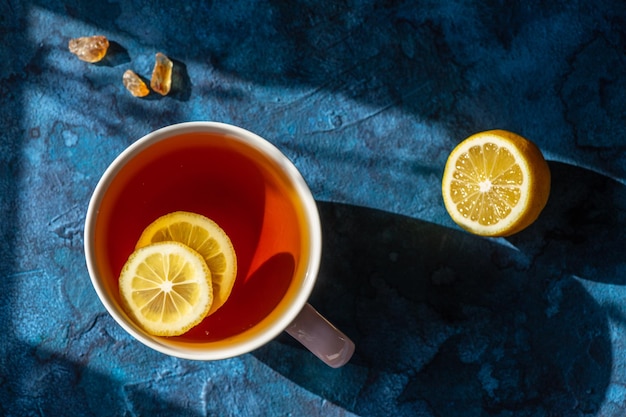 Une tasse avec du thé et des tranches de citron flottant dedans sur fond bleu