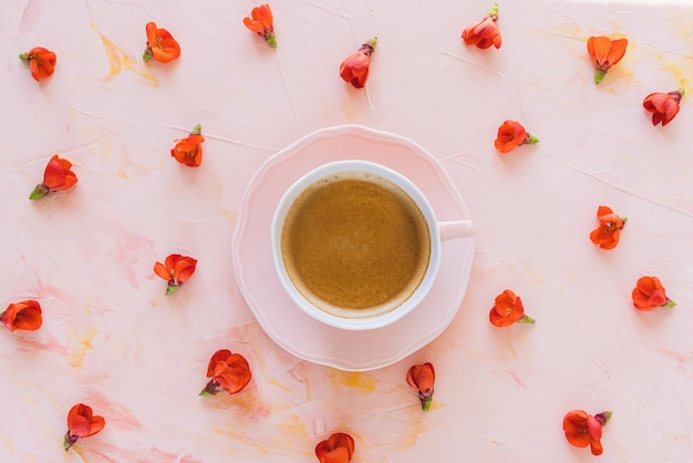 Tasse d'espresso avec crème et fleurs rouges fraîches sur fond rose buvant du café en été ou