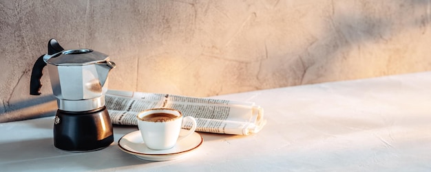 Une tasse d'expresso une cafetière et un journal au soleil du matin