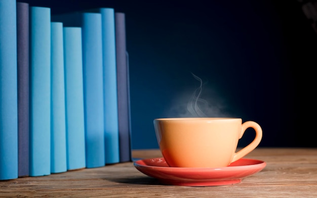 Tasse jaune de café ou de thé avec de la vapeur chaude sur des livres bleu clair en bois de table et fond bleu