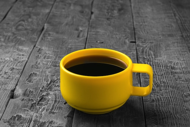 Une tasse jaune avec du café noir sur une table en bois. Une boisson chaude revigorante.