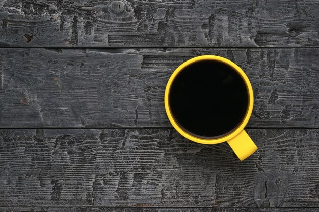 Une tasse jaune avec du café noir sur une table en bois noire.