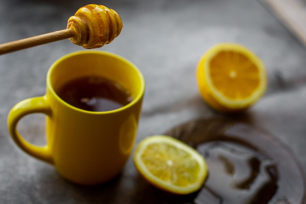 tasse jaune, gouttes de miel sur une soucoupe, fond gris au citron