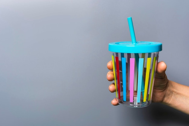 Une tasse de jus de couleur avec une paille dans une main de femme sur un fond gris une main avec une tasse en plastique