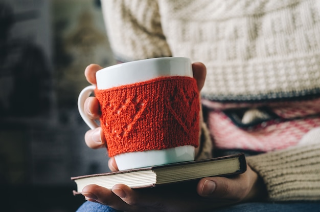 Tasse en laine tricotée rouge avec motif coeur en mains féminines.