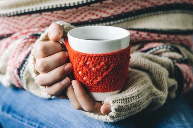 Tasse en laine tricotée rouge avec motif coeur en mains féminines.