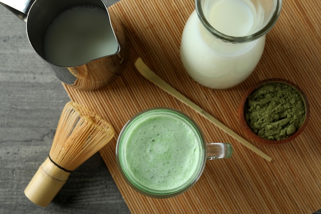 Tasse de matcha latte et accessoires pour faire sur une table texturée grise