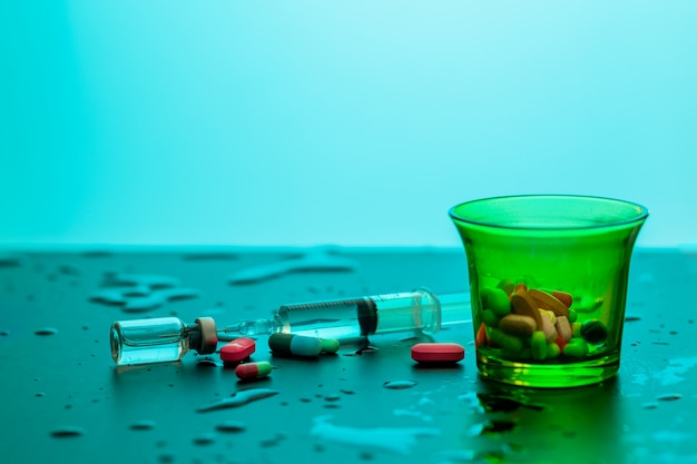 Tasse à mesurer de couleur verte avec les comprimés à l'intérieur d'une seringue numérotée avec un médicament se trouvant entre des gouttes d'eau. Concept de santé.