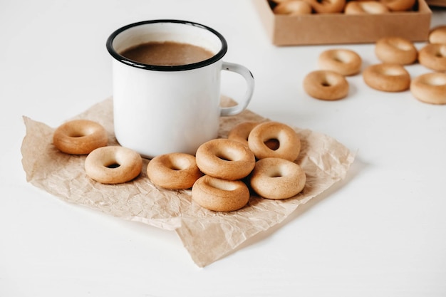 Tasse en métal avec boisson chaude et mini bagels ronds sur fond de bois blanc