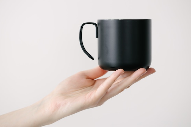 Tasse en métal noir pour le thé et le café à la main de la femme