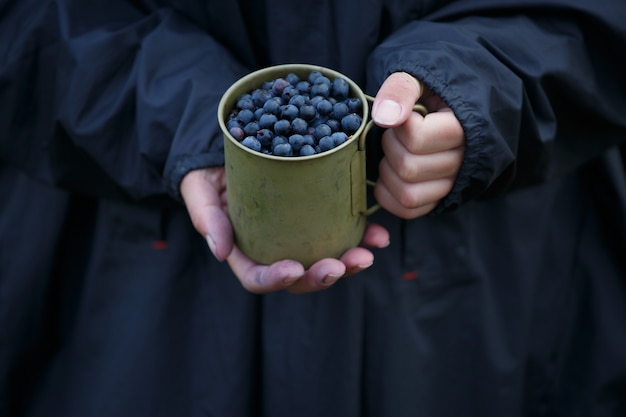 Tasse en métal pleine avec des bleuets frais dans les mains