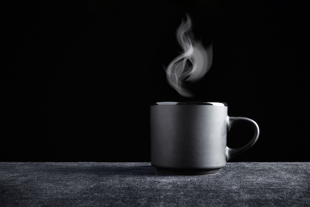 Tasse noire avec de la vapeur dessus sur une surface sombre et un fond noir.