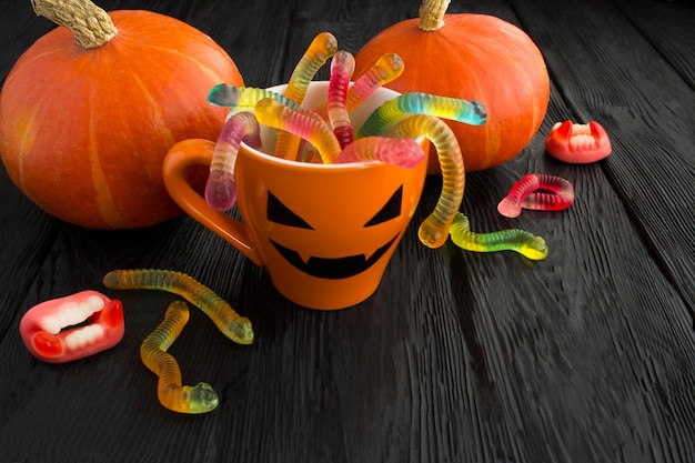 Tasse orange avec des bonbons pour Halloween et citrouilles à côté