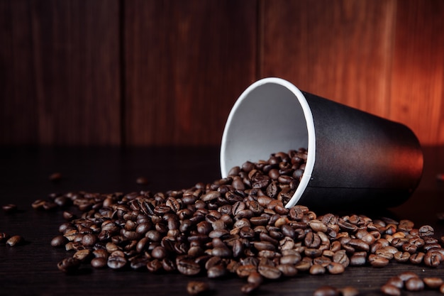 Une tasse de papier de café avec des grains de café sur une surface en bois