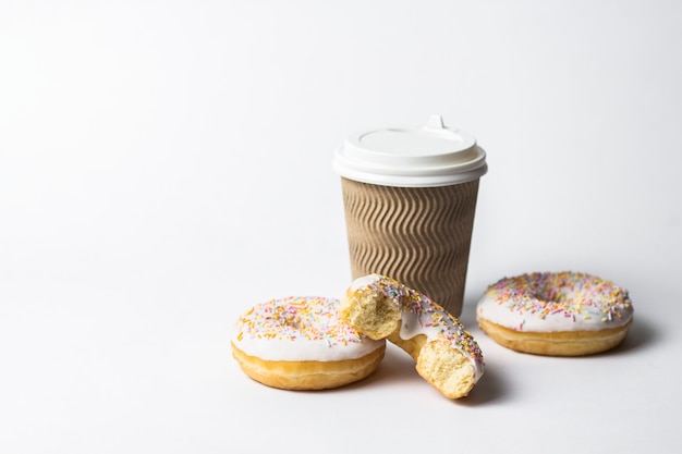 tasse en papier avec un couvercle, du café ou du thé à emporter et des beignets savoureux frais et des bonbons décoratifs multicolores sucrés sur fond blanc. Concept de boulangerie, pâtisseries fraîches, délicieux petit déjeuner, restauration rapide.