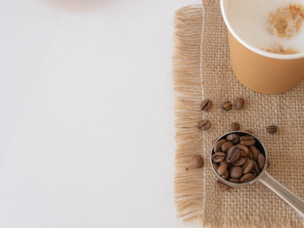 Une tasse de papier jetable avec cappuccino sur une serviette en toile grains et café moulu sont éparpillés sur la table et une cuillère de service Vue de dessus Espace pour copier