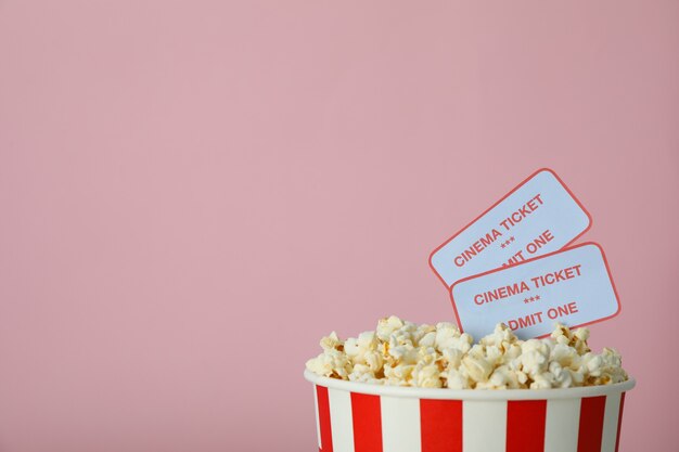 Tasse en papier avec pop-corn et billets sur fond rose.