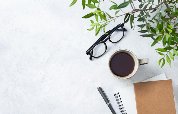 Tasse à plat de thé artisanal bloc-notes stylo et lunettes sur un fond clair avec des branches vertes gros plan Concept féminin de printemps Vue de dessus et espace de copie