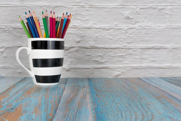 Tasse rayée pleine de crayons de couleur sur un joli fond avec espace de copie