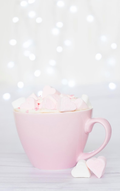 Tasse rose avec des guimauves en forme de coeurs sur fond de lumières