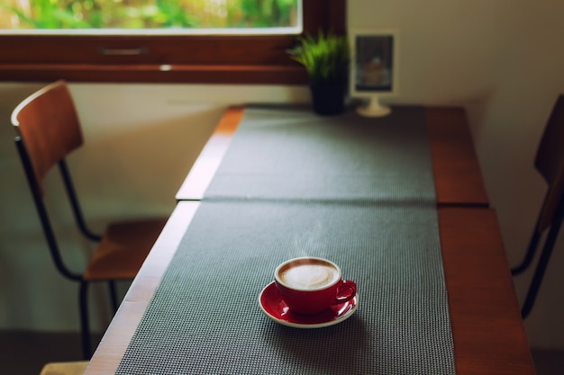 Tasse rouge, café au lait en forme de coeur sur une nappe en bois