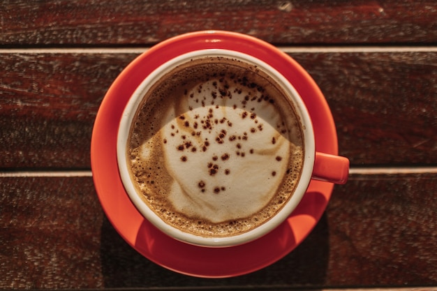 Tasse rouge de café latte chaud sur table en bois tôt le matin.