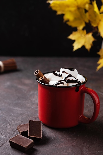 Tasse rouge de chocolat chaud aromatique avec des guimauves et de la cannelle et des feuilles d'érable d'automne sur fond marron Concept boisson confortable Vue de face et espace de copie