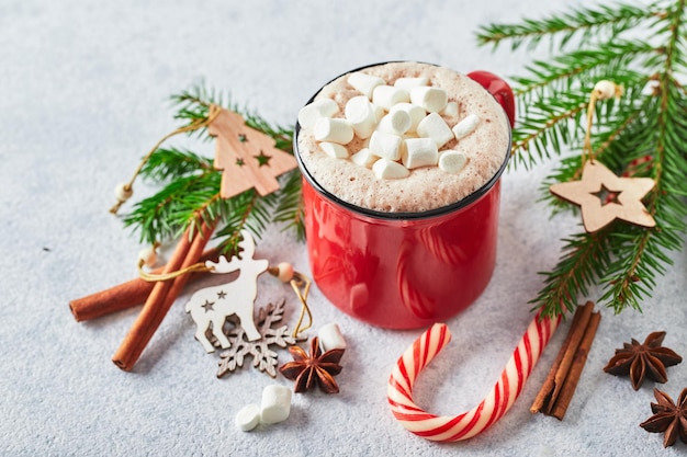 Tasse rouge de chocolat chaud avec des guimauves et des cannes de bonbon avec arbre de noël