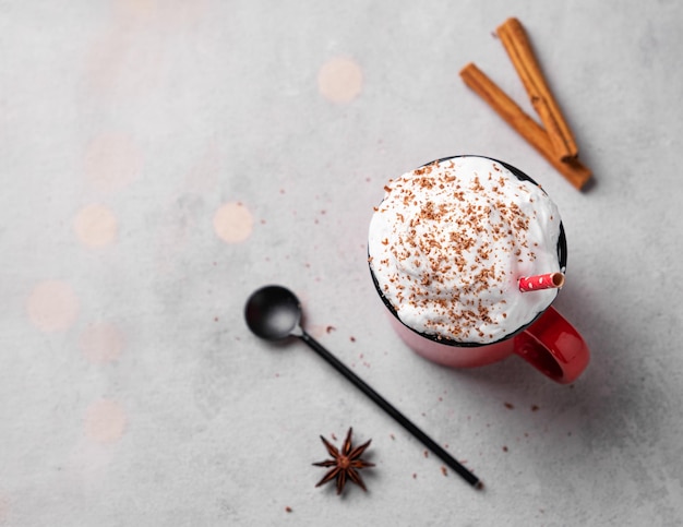 Une tasse rouge avec du chocolat chaud ou du cacao avec de la crème fouettée avec une cuillère de bâtons de cannelle et d'anis étoilé