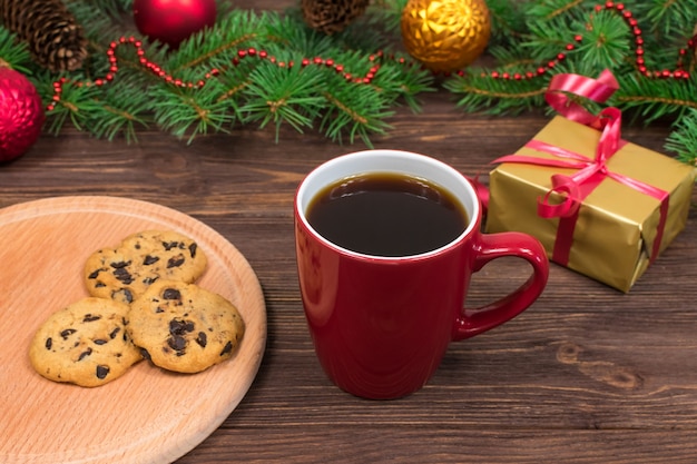 Tasse rouge avec du thé, du café avec des biscuits et des guimauves sur une table en bois dans le contexte d'un arbre du Nouvel An avec des décorations de Noël.