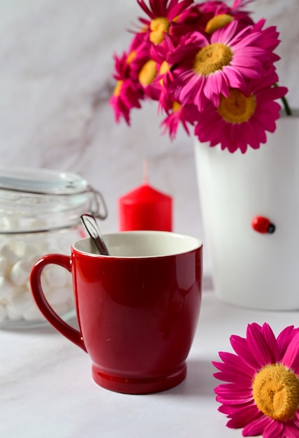 Tasse rouge avec du thé sur le fond d'un bouquet de fleurs rouges