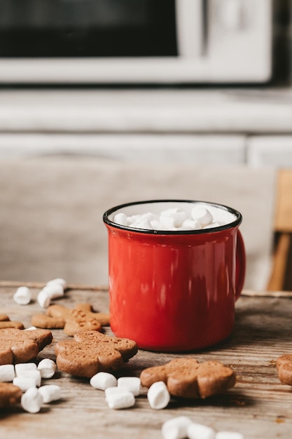 Tasse rouge avec gros plan de cacao et de guimauves sur un fond en bois. Biscuits de Noël et autres douceurs au cacao