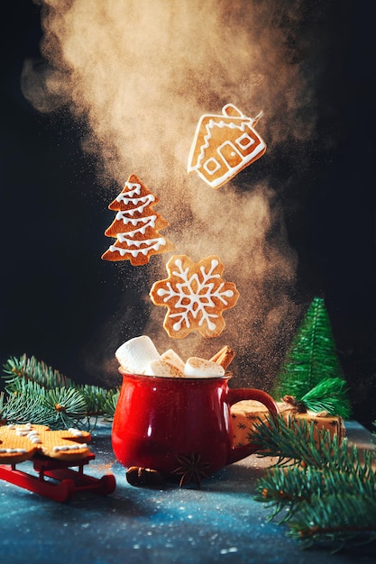 Tasse rouge avec des guimauves et de la cannelle et des biscuits de pain d'épice de Noël volants