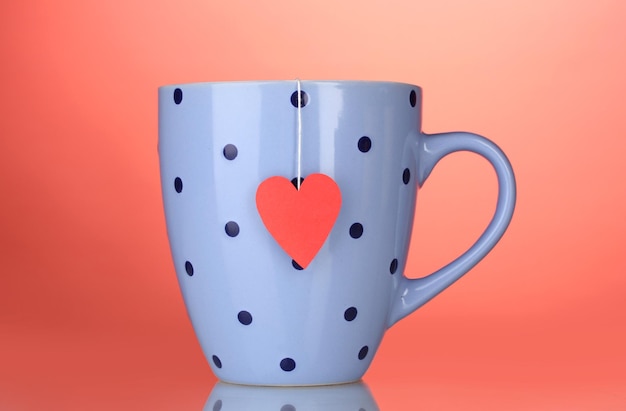 Tasse et sachet de thé bleus avec étiquette en forme de coeur rouge sur fond rouge