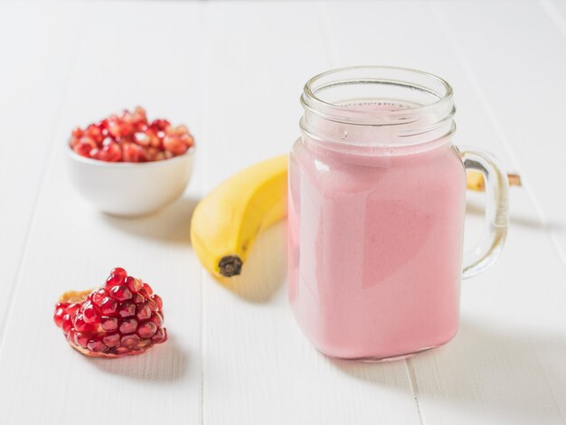 Une tasse de smoothie banane grenade et fruits frais sur un tableau blanc. Menu végétarien.